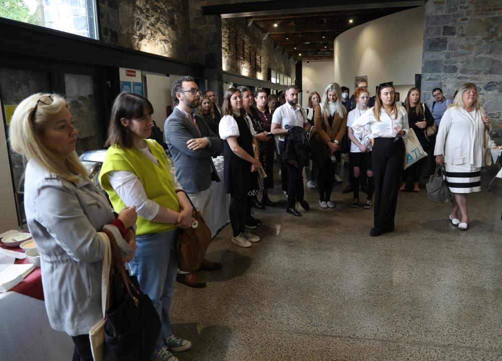 Photograph of attendees at Practitioners Forum standing in a semi-circle listening to Ciarán Ó hÓgartaigh